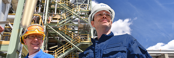 Two engineers outside plant with blue sky and white clouds in the background